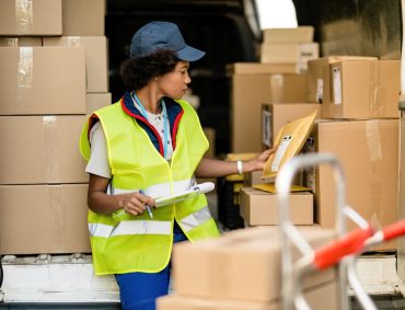 Black female courier working and checking packages in a delivery van.